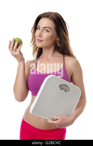 Pretty young fitness model holding a green apple and some weight scales isolated over white background Stock Photo