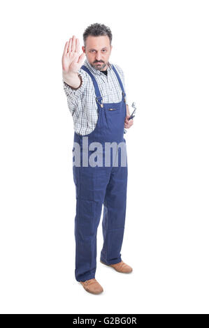 Serious mechanic in overalls making a stop gesture while holding spanner isolated on white background Stock Photo