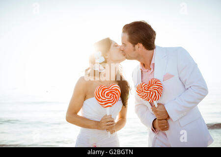 Bride and groom kissing, heart-shaped lollipops in their hands, Spain Stock Photo