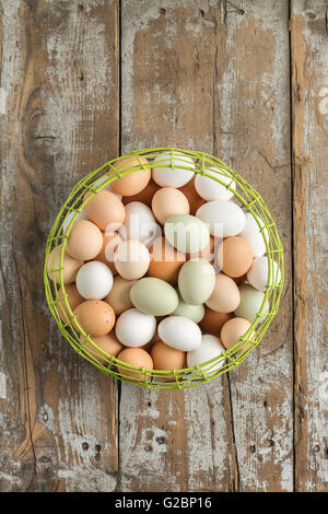 Colorful eggs in a wire basket on a rustic wooden surface. Stock Photo