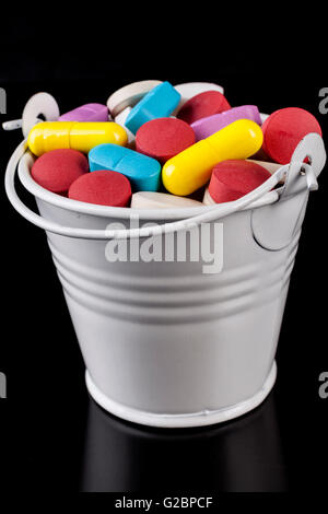 Colored pills medicine in a white bucket isolated on black background Stock Photo