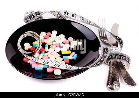 Silver fork and knife on colored pills in  black plate with measuring tape isolated on white background Stock Photo