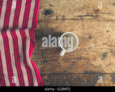 Overhead shot of empty cup and red and white tea towel on a wooden surface Stock Photo