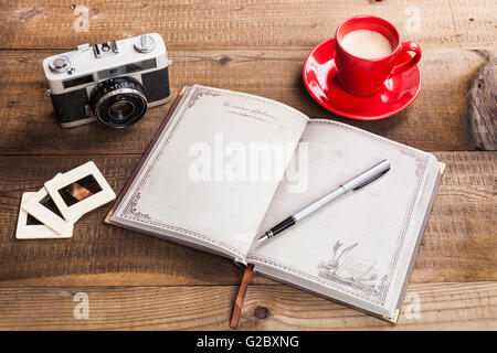 Old Camera Closeup on Brown Wood Background With Open Notepad and Coffee in Red Mug Stock Photo