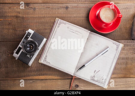 Old Camera Closeup on Brown Wood Background With Open Notepad and Coffee in Red Mug Stock Photo