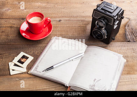 Old Camera Closeup on Brown Wood Background With Open Notepad and Coffee in Red Mug Stock Photo