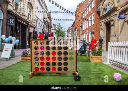 Disc‑dropping fun with the classic game of Connect 4, or 6;  Connect Four also known as Captain's Mistress, Four Up, Plot Four, Find Four, Four in a Row, Four in a Line, Drop Four, and Gravitrips, dropping your red discs in the wooden grid. May Spring Bank Holiday in Manchester's central business district celebrating the past, present, and future of King Street. Stock Photo