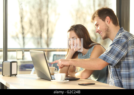 Profile of a happy couple searching information on line together connected in a laptop inside a coffee shop Stock Photo