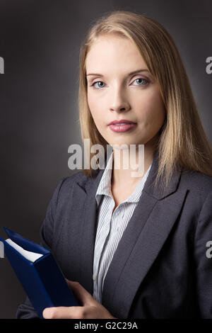 Close up portrait studio shot of a smart business woman wearing a suit, holding a blue folder.  Shot on a grey background. Stock Photo