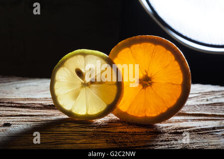 Slices of orange and lemon glowing with translucent light with light source at the background on rough wooden surface Stock Photo