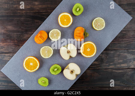 Slices of fruits on chopping board. Apples, lemons, oranges, kiwi, and persimmon. Top view. Stock Photo