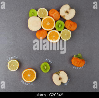Slices of fruits with handwritten lables on stone surface. Lemon, orange, kiwi, apple, persimmon. Top view