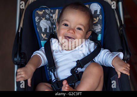 little baby boy sitting in a stroller in the home, ready for a walk in a pram Stock Photo