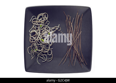 Cooked and raw organic Black Bean Spaghetti on black plate Stock Photo