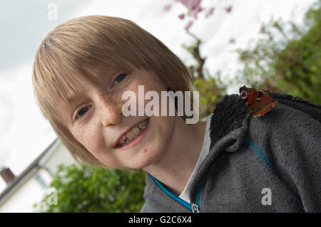 Boy with peacock butterfly (Aglais io) sitting on his shoulder Stock Photo