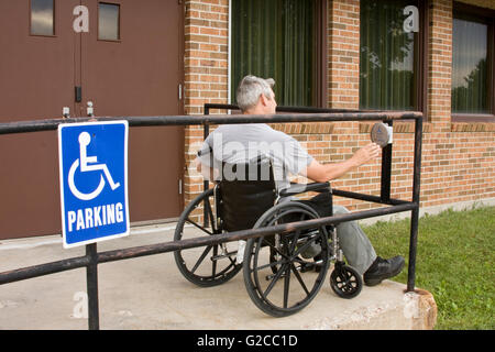 disabled man in a wheelchair pushing a handicapped entrance button Stock Photo