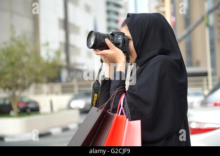 Emarati Arab woman coming out of shopping and taking photo with her camera in Dubai, United Arab Emirates. Stock Photo