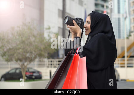 Emarati Arab woman coming out of shopping and taking photo with her camera in Dubai, United Arab Emirates. Stock Photo