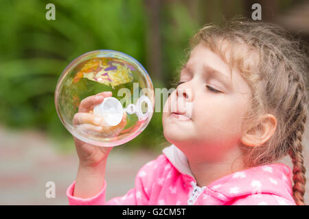 Five-year girl inflates a large circular bubble Stock Photo