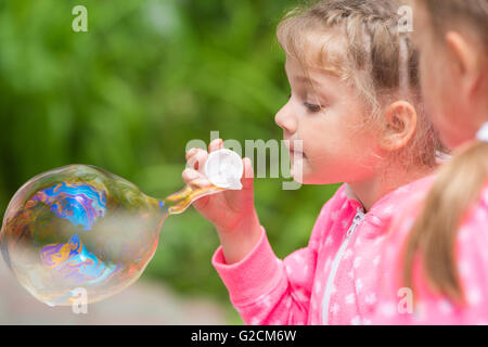 Five-year girl inflates a large bubble, another girl with interest looks at her Stock Photo