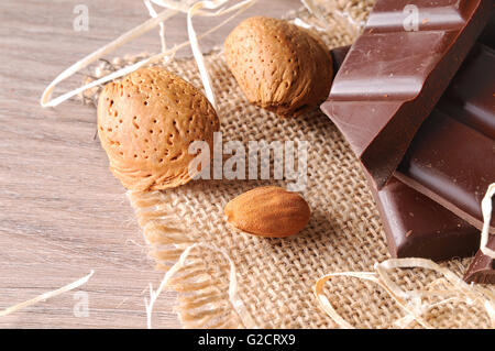 Heap of artisan portions chocolate on burlap sack with almonds on a brown wooden table with straw decoration. Horizontal Stock Photo