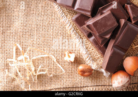 Heap of artisan portions chocolate on burlap sack with hazelnuts with straw decoration. Horizontal composition. Top view. Stock Photo
