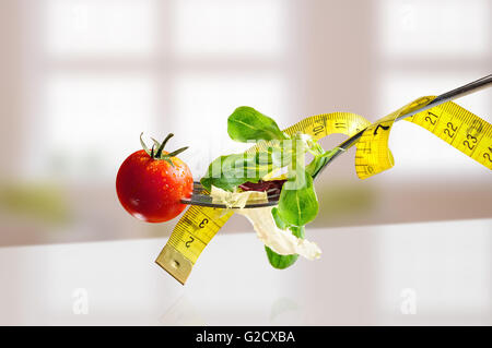 Salad with lettuce and tomato on a metal fork with tape on white table and windows background. Concept healthy diet, nutrition Stock Photo