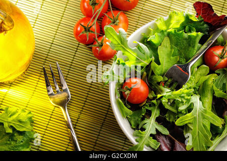 salad in a bowl on bamboo tablecloth with fork and oil, top view Stock Photo