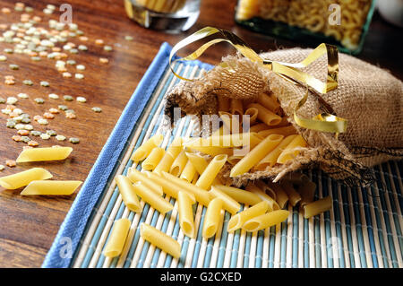uncooked macaroni composition out of a burlap sack on a blue tablecloth Stock Photo
