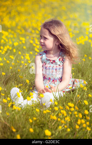 3 year old girl sitting in a meadow with yellow flowers Stock Photo