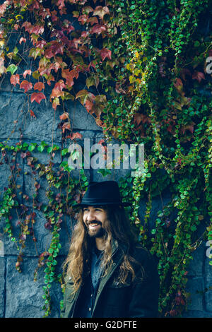Portrait of Smiling Man with Beard and Long Hair Standing Against Vine-Covered Wall Stock Photo