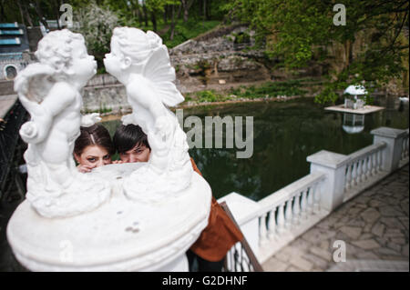 Couple hiding from statue of two kissing cupids angels Stock Photo