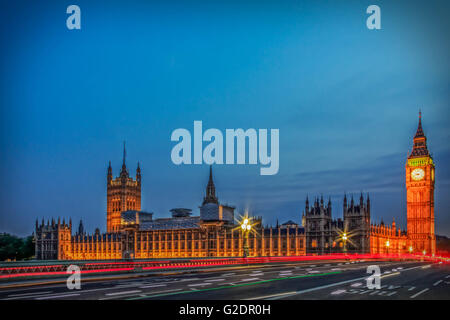 Palace of Westminster in London, and the Big Ben at night with vehicle leaving a trail along the road, with a clear blue sky. Stock Photo