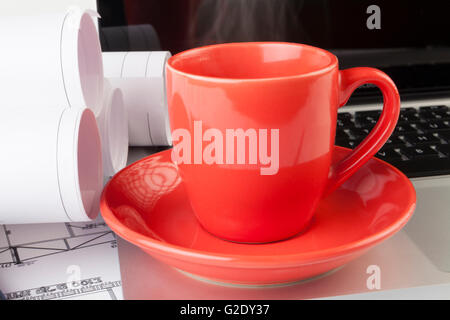 Architect drawing blueprints with a silver laptop with red steaming cup of coffee Stock Photo