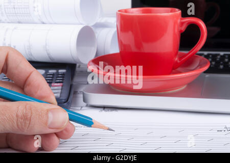 Architect drawing blueprints with a calculator ans a silver laptop with pencil and red cup of coffee Stock Photo