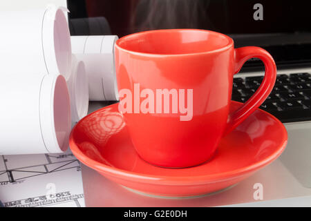 Architect drawing blueprints with a silver laptop with red steaming cup of coffee Stock Photo