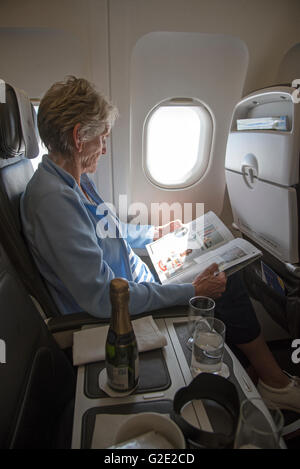 An elderly lady passenger seated by an aircraft window reading a magazine Stock Photo