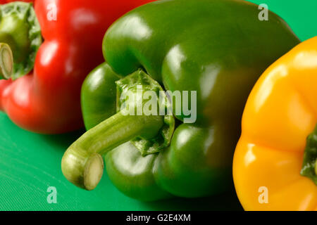 Red, green and yellow bell peppers on green chopping board - the correct colour board for food hygiene requirements Stock Photo