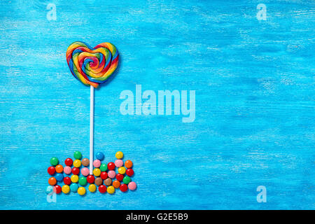 flat lay of beautiful multicolored lollipop shape heart and sweet bonbons on painted blue wooden background, close up Stock Photo