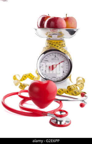 Red apple with  yellow measuring tape on kitchen scale with red heart and stethoscope isolated on white Stock Photo