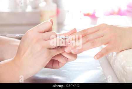 Nail manicure pedicure salon. Beautician is doing cuticles care with cuticle pusher for the client. Stock Photo