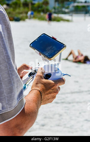 A man's hands holding a radio controller with joysticks piloting an unseen non-military drone flying overhead at the beach Stock Photo