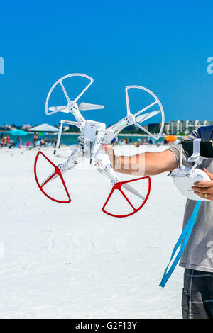 A man holds a non-military drone sideways at the beach with radio controller in other hand Stock Photo