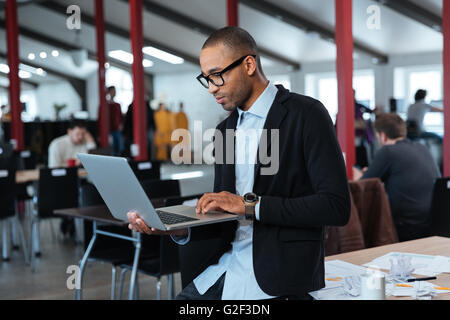 Serious smart businessman is standing and using laptop at the office Stock Photo
