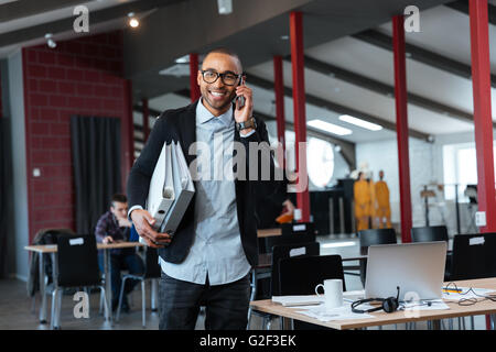 Young businessman talking on the cellphone and carrying binders in the office Stock Photo