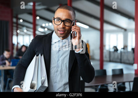 Young bisnessman carrying folders and talking on the phone in the office Stock Photo