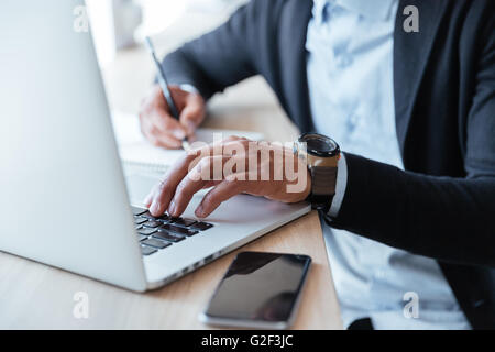 Close-up portrait of multitasking mans hands using laptop and writing notes Stock Photo