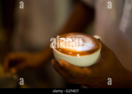 How to make latte art coffee. Hands holding a cup of coffee with foam over wooden table, side view Stock Photo