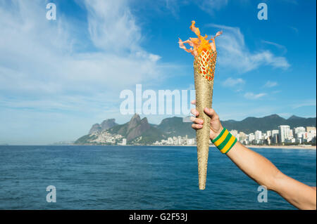 Hand of an athlete wearing Brazil colors sweatband holding sport torch against Rio de Janeiro Brazil skyline Stock Photo