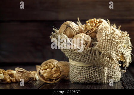 Walnuts in small burlap bag on dark wooden background. Copy space Stock Photo
